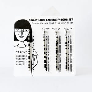 Może przedstawiać: Zestaw czterech wiszących kolczyk&oacute;w na białej karcie ekspozycyjnej z napisem BINARY CODE EARRING F-BOMB SET. Każdy kolczyk składa się z pionowego sznurka naprzemiennie ułożonych czarnych i srebrnych koralik&oacute;w oraz tekstu w kodzie binarnym.