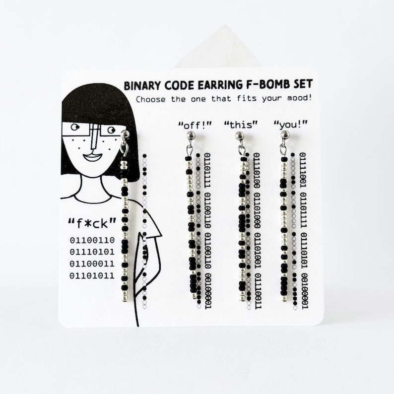 Może przedstawiać: Zestaw czterech wiszących kolczyk&oacute;w na białej karcie ekspozycyjnej z napisem BINARY CODE EARRING F-BOMB SET. Każdy kolczyk składa się z pionowego sznurka naprzemiennie ułożonych czarnych i srebrnych koralik&oacute;w oraz tekstu w kodzie binarnym.