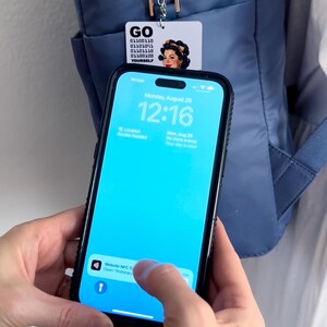 Peut inclure: Un smartphone avec un &eacute;cran bleu vif affichant une notification pour une balise NFC de site web, plac&eacute; devant un sac &agrave; dos bleu. Une petite &eacute;tiquette rectangulaire blanche est suspendue au sac, avec le texte GO, du code binaire et une illustration.