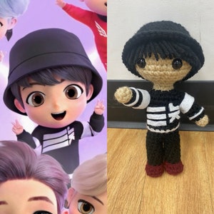 May include: A crocheted plush toy of a person wearing a black and white striped shirt, black pants, and a black hat. The toy has brown eyes and a brown crocheted face.