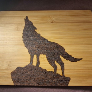 Op de afbeelding: Een houten snijplank met een lasergegraveerd silhouet van een wolf die huilt naar de maan. De wolf is donkerbruin en de plank is lichtbruin.