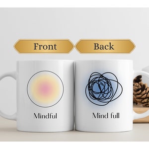 May include: Two white ceramic mugs. One mug has a yellow and pink gradient circle with the word "Mindful". The other mug has a black scribble design with the words "Mind full".