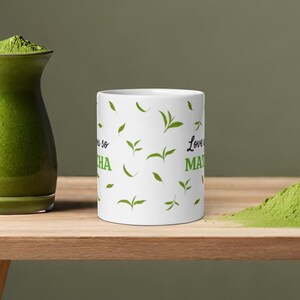 Peut inclure: Une tasse en c&eacute;ramique blanche avec un motif de feuilles vertes et le texte "Love you so matcha" imprim&eacute; dessus.
