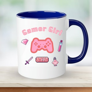 Op de afbeelding: Een witte keramische mok met een blauwe rand en handvat. De mok heeft een roze gamer girl-ontwerp met een roze videogamecontroller, een roze diamant, een roze zwaard, een roze drankfles en een roze drankfles met een roze ster erop. De tekst "Gamer Girl" staat in roze letters op de mok.