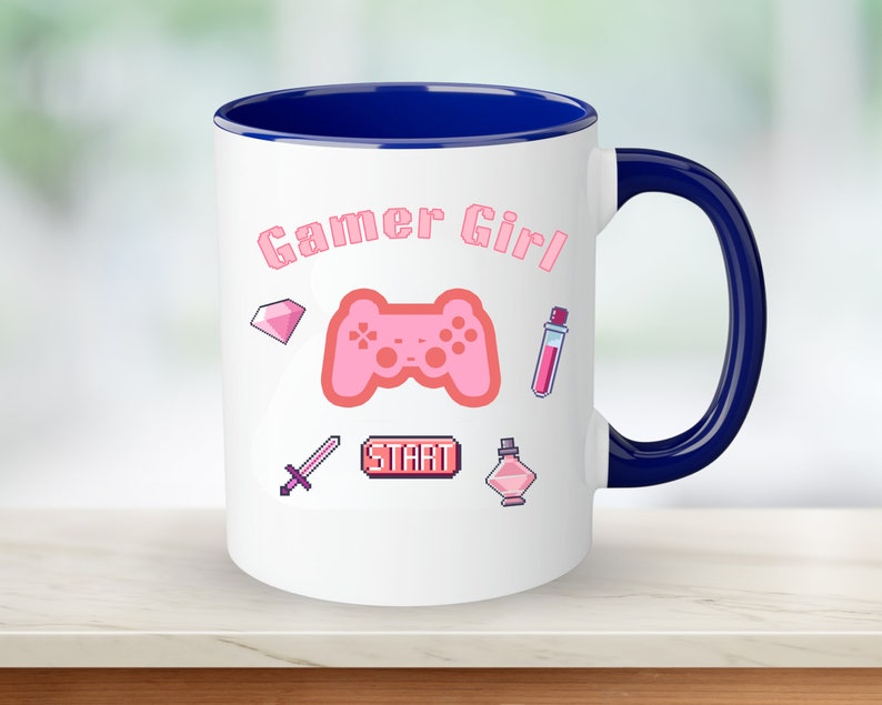 Op de afbeelding: Een witte keramische mok met een blauwe rand en handvat. De mok heeft een roze gamer girl-ontwerp met een roze videogamecontroller, een roze diamant, een roze zwaard, een roze drankfles en een roze drankfles met een roze ster erop. De tekst "Gamer Girl" staat in roze letters op de mok.