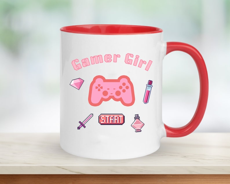 Op de afbeelding: Witte keramische mok met een rode rand en handvat. De mok heeft een roze gamer girl-ontwerp met een roze videogamecontroller, een roze diamant, een roze zwaard, een roze drankfles, een roze parfumfles en een roze "START"-knop.