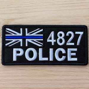 May include: A rectangular black embroidered patch featuring a stylised Union Jack flag with a horizontal blue line across the centre. To the right of the flag, the white embroidered number 4827 is displayed above the white text POLICE.