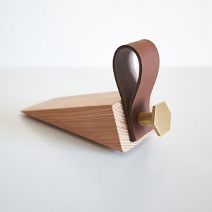 Könnte beinhalten: Ein Holz-Türstopper mit einem braunen Leder-Schlaufen-Griff und einem sechseckigen Messingknopf.