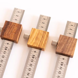Könnte beinhalten: Drei Holz-Anreißwinkel mit Metalllinealen. Die Holzblöcke sind in verschiedenen Braun- und Beigetönen gehalten. Die Lineale sind in Zentimetern markiert, bis zu 40 cm.