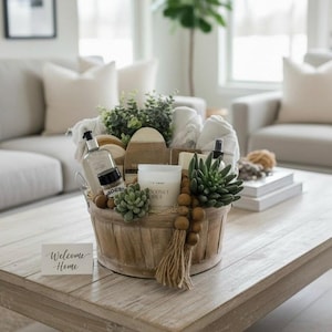 May include: A wooden basket filled with spa-themed items sits on a light-colored wooden coffee table. The basket contains a candle, soaps, lotions, and decorative succulents. A small card with the words "Welcome Home" is in front of the basket.