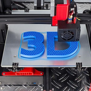 Op de afbeelding: Een 3D-printer in werking, die de letters "3D" in blauw print. De printer heeft een zwart frame met rode accenten en een zilveren printbed. De letters zijn gemaakt van een blauw roosterachtig materiaal.