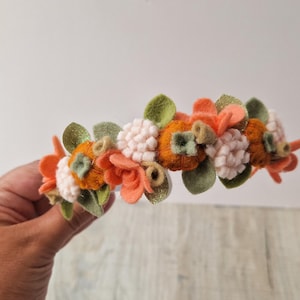 May include: A felt headband decorated with orange, green and white felt flowers. The headband is ideal for autumn.