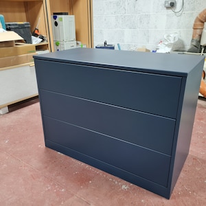 May include: A dark blue chest of drawers with three drawers. The chest of drawers is made of wood and has a simple, modern design.