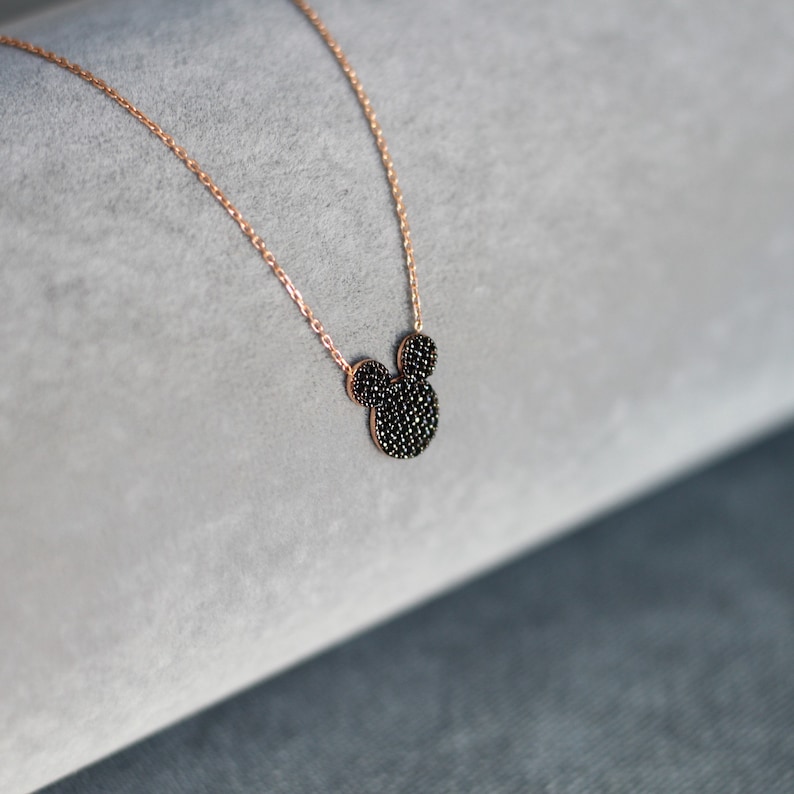 K&ouml;nnte beinhalten: Eine zarte goldene Kettenkette mit einem schwarzen, funkelnden Mickey Mouse Anh&auml;nger.