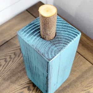 May include: A teal blue wooden block with a round hole in the top. A natural wood dowel is inserted into the hole.