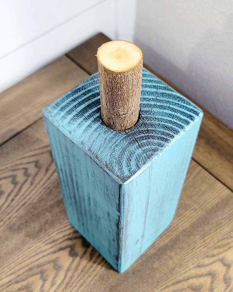May include: A teal blue wooden block with a round hole in the top. A natural wood dowel is inserted into the hole.