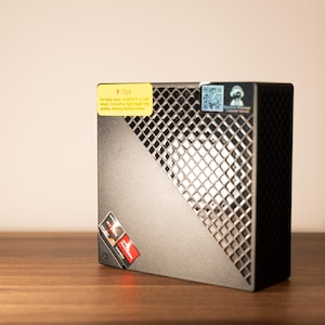 May include: A black computer component with a diamond-patterned grill and a yellow sticker that reads "Tips". The component has a red and white sticker that says "Ryzen" and "Radeon Graphics".