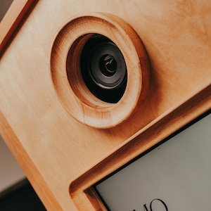 Può includere: Un foto booth in legno con un obiettivo della fotocamera e uno schermo che mostra il testo "MO MINT. booth".