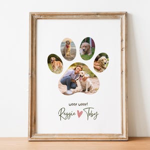 May include: A framed wall art print featuring a collage of five dog photographs arranged in the shape of a paw print. Below the paw print, the text reads WOOF WOOF! followed by the names Reggie and Toby separated by a small pink heart.