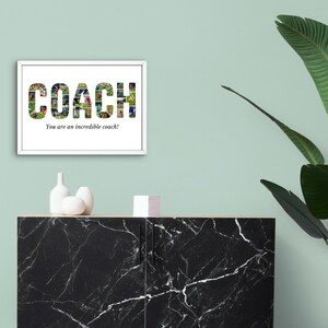 K&ouml;nnte beinhalten: Ein wei&szlig; gerahmtes Foto mit dem Wort "COACH", das in Gr&uuml;n und Rot mit einer Collage von Fotos ausgeschrieben ist. Der Text "You are an incredible coach!" befindet sich unter dem Wort "COACH". Das Foto h&auml;ngt an einer hellgr&uuml;nen Wand &uuml;ber einem schwarzen Marmorschrank.