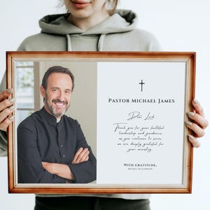 May include: A wooden framed portrait of Pastor Michael James. The left side shows a smiling man in a black clerical shirt. The right side has text including "Dear Lord" and "Thank you for your faithful leadership and guidance."
