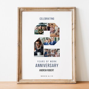 以下が含まれることがあります： アンドリュー・ロバートのMerck & Co.での2周年記念を祝う額装されたポスター。ポスターには、職場環境にいる人々の写真のコラージュが、数字の2の形に配置されています。