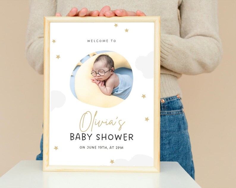 K&ouml;nnte beinhalten: Eine Babyparty-Einladung mit wei&szlig;em Hintergrund und goldenen Sternen. Die Einladung zeigt ein Foto eines Babys, das auf einem gelben Halbmond schl&auml;ft. Der Text lautet "Willkommen zur Babyparty von Olivia am 19. Juni um 14:00 Uhr."