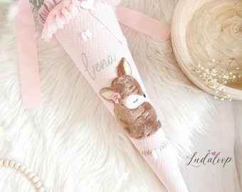 May include: Pink and white school cone with a deer applique and the name "Lena" embroidered on the side. The cone is decorated with lace and a white heart.