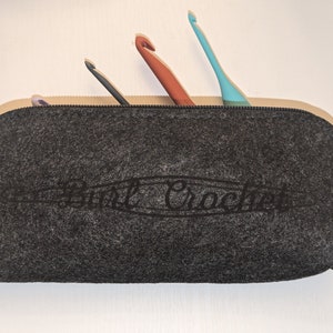 May include: A grey felt crochet hook case with a zipper closure and the text "purl crochet" embroidered on the front.