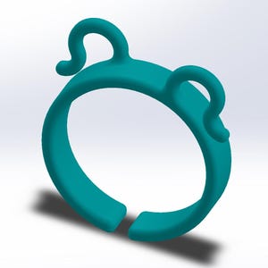 Op de afbeelding: Turquoise blauwe plastic ring met twee kleine lussen aan de bovenkant. De ring is ontworpen om een telefoon of ander apparaat vast te houden.