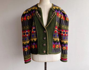 May include: A green, red, yellow, purple, and black patterned cardigan with silver heart-shaped buttons. The cardigan has a V-neck and long sleeves.