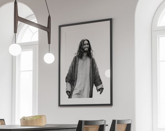 Op de afbeelding: Zwart-wit ingelijste print van een persoon met lang haar en een baard, gekleed in een gewaad. De print wordt weergegeven op een witte muur in een kamer met een donkere tafel en stoelen. Twee bolvormige hanglampen hangen aan het plafond.