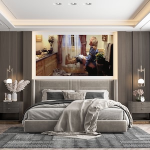 May include: A bedroom interior with a large framed print of a man sitting on a toilet. The print is hanging on a wall with a dark brown wood paneling. The bed is made with a gray duvet and a white throw blanket. There are two nightstands with lamps on either side of the bed.