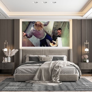 K&ouml;nnte beinhalten: Ein modernes Schlafzimmer mit einem grauen Kopfteil und einer grauen Bettdecke. Der Raum hat einen gro&szlig;en gerahmten Druck von zwei Personen in einem Badezimmer, einen grauen Teppich und zwei Nachttische mit Lampen.