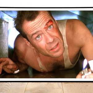 May include: A man with a bloody face is crawling through a vent. He is wearing a white tank top and has a lighter in his hand.