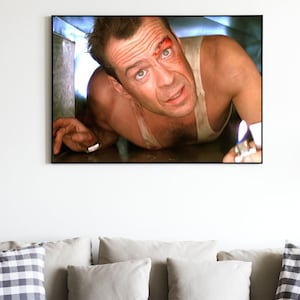 May include: A close-up of a man's face with a bloody cut on his forehead. He is wearing a white tank top and is holding a lighter with a flame. The image is from the movie "Die Hard with a Vengeance".