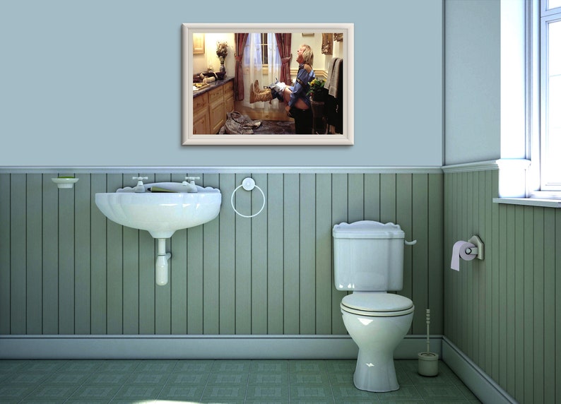 May include: A framed picture of a bathroom with a person sitting on the toilet. The picture is hanging on a light blue wall with white trim. The bathroom has a white sink and a white toilet.
