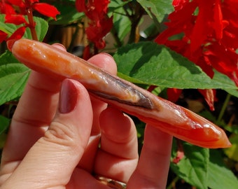 May include: A long, thin, orange and brown carnelian crystal wand with a pointed tip.