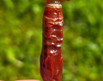 May include: A red and white banded agate stone with a smooth, polished surface. The stone is shaped like a long, thin tower.
