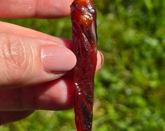 May include: A long, thin, red and white agate point with a white tip. The agate has a swirling pattern and is translucent.