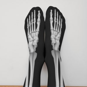 May include: A pair of black socks with a white skeleton foot design. The socks are pulled up to the ankles and the feet are visible.