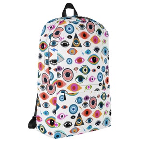 Puede incluir: Una mochila blanca con un patr&oacute;n colorido de ojos y tri&aacute;ngulos. Los ojos son de varios colores, incluyendo azul, verde, rojo y naranja. Los tri&aacute;ngulos son negros y blancos.