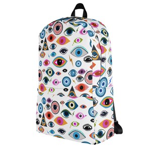 Puede incluir: Una mochila blanca con un patr&oacute;n de ojos coloridos. Los ojos son de varias formas, tama&ntilde;os y colores, incluyendo azul, verde, naranja y rosa. La mochila tiene correas negras y un cierre de cremallera.