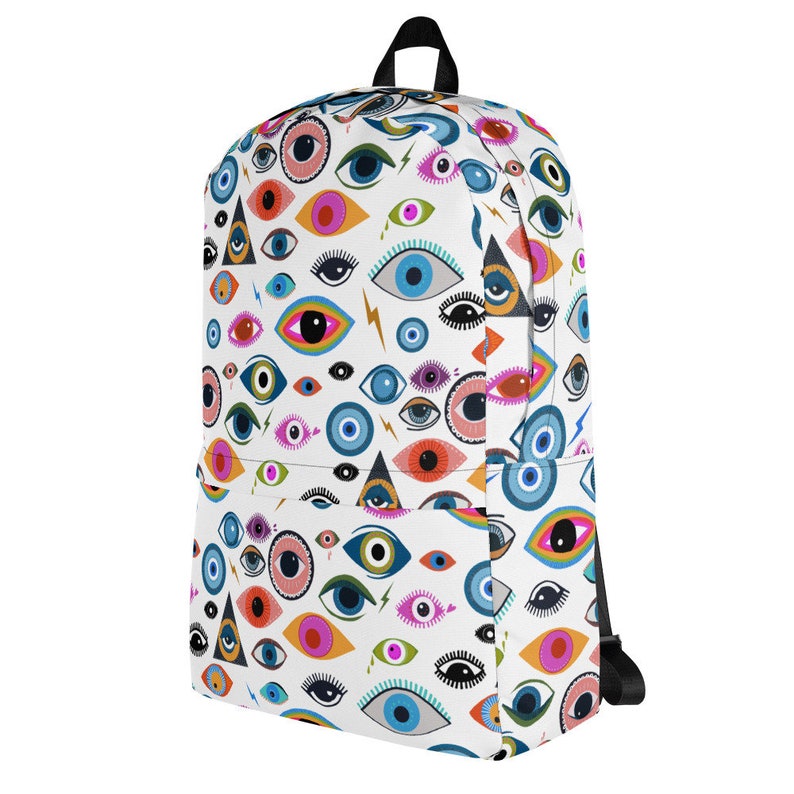 Puede incluir: Una mochila blanca con un patr&oacute;n de ojos coloridos. Los ojos son de varias formas, tama&ntilde;os y colores, incluyendo azul, verde, naranja y rosa. La mochila tiene correas negras y un cierre de cremallera.