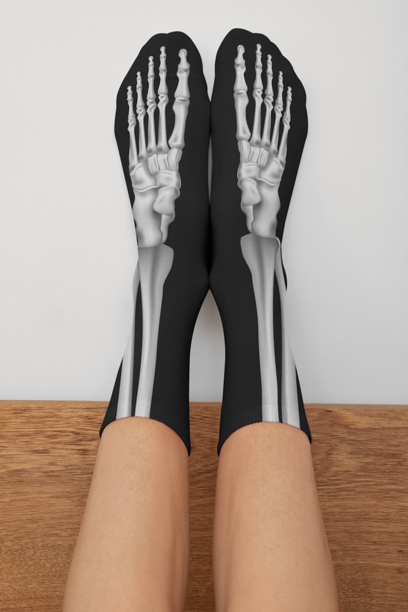 May include: A pair of black socks with a white skeleton foot design. The socks are pulled up to the ankles and the feet are visible.
