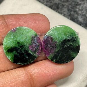Peut inclure: Deux pierres précieuses rondes avec un mélange de couleurs vertes, noires et magenta. Les pierres ont une surface polie et un aspect naturel et organique. Les pierres sont probablement destinées à la création de bijoux.