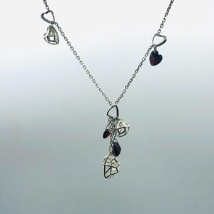 Può includere: Una collana a catena d'argento con più ciondoli a forma di cuore d'argento. Alcuni dei cuori hanno pietre preziose rosse all'interno.