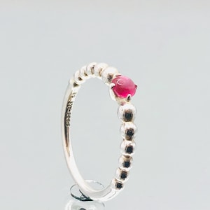 May include: A silver ring with a beaded band and a single red gemstone. The ring is marked "S925 ALE 925".