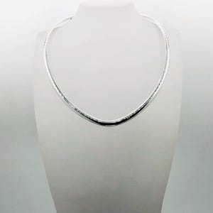 May include: A polished silver-tone omega chain necklace featuring a smooth, rounded, and semi-rigid design that sits in a circular shape. The necklace has a reflective metallic surface with a consistent thickness throughout the entire band.