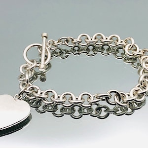 May include: A silver chain bracelet with a heart-shaped charm. The bracelet has a toggle clasp.